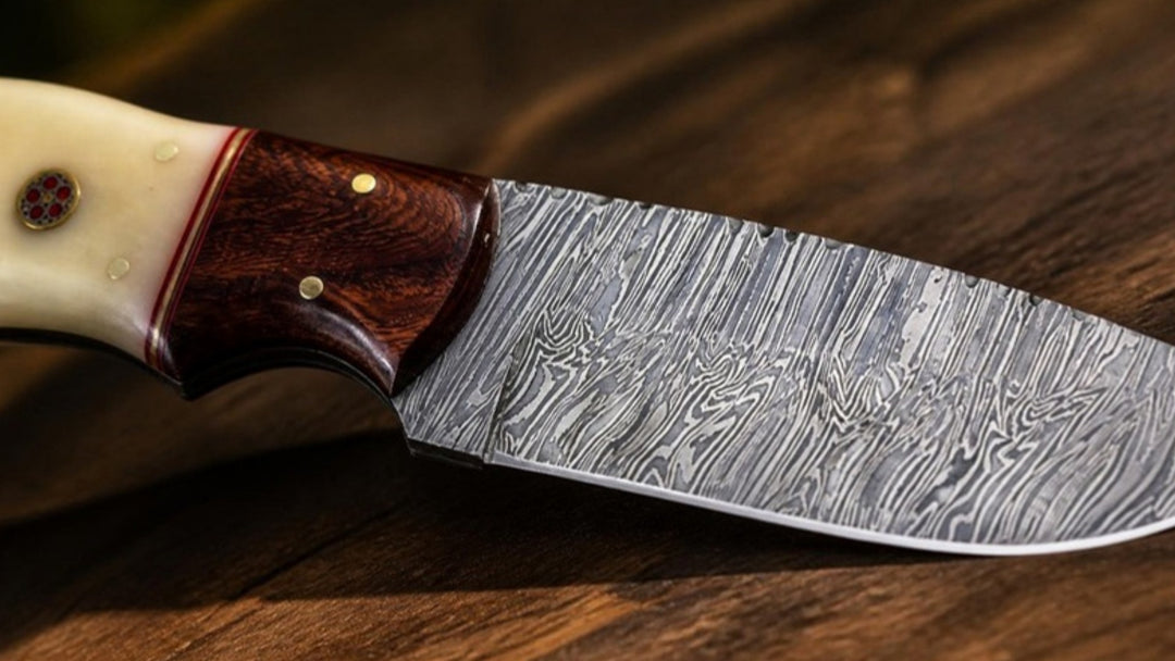 Close-up of the layered Damascus steel pattern on a hand-forged hunting knife with rosewood bolster and camel bone handle