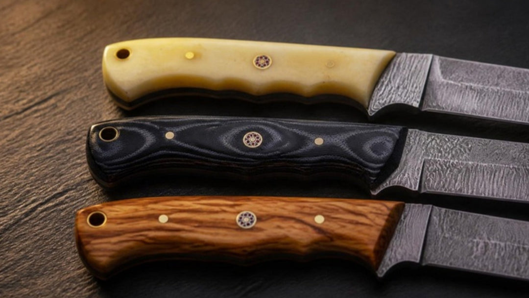 Close-up of three Damascus knife handles in bone, black Micarta and olive wood laid side by side on slate